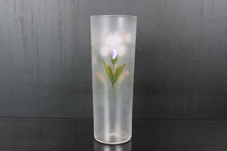 Pu&ograve; includere: Un vaso di vetro smerigliato con un motivo floreale dipinto. Il motivo presenta un fiore viola con foglie verdi e dettagli dorati. Il vaso &egrave; cilindrico e ha una finitura liscia e smerigliata.