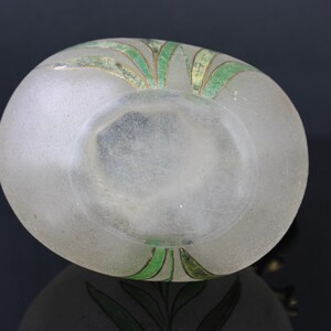 May include: A frosted glass bottle with a green and gold floral design. The bottle is clear and has a textured surface.