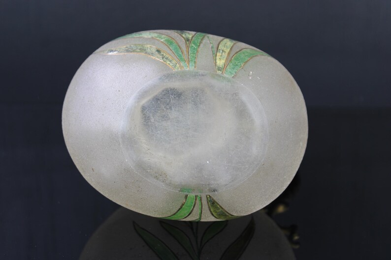 May include: A frosted glass bottle with a green and gold floral design. The bottle is clear and has a textured surface.