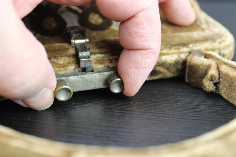 May include: Close-up of a vintage brown velvet purse with a metal clasp and two metal buttons. The purse is closed and the clasp is secured.