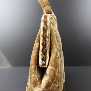 May include: A brown velvet handbag with a quilted pattern and a top handle. The handbag has a decorative trim along the top edge.