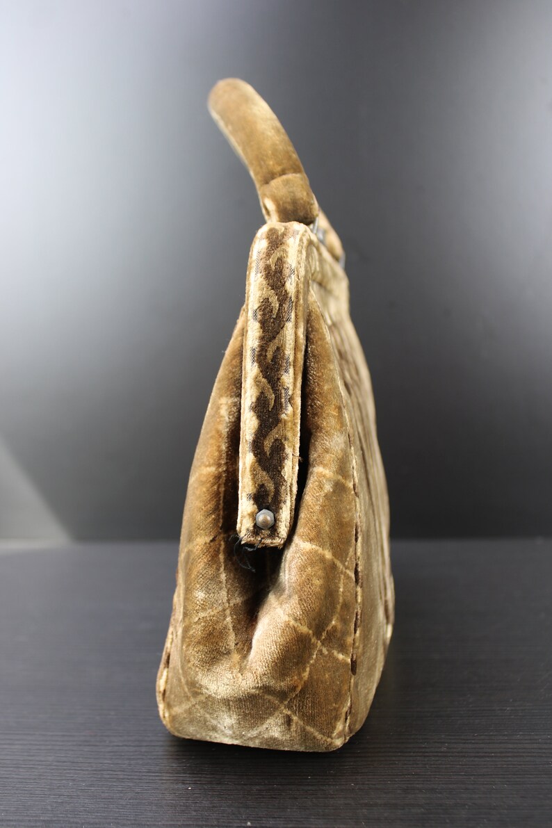 May include: A brown velvet handbag with a quilted pattern and a top handle. The handbag has a decorative trim along the top edge.