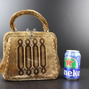 May include: A small, brown velvet handbag with a geometric design and a silver clasp. The bag is about the size of a can of beer.