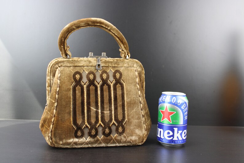 May include: A small, brown velvet handbag with a geometric design and a silver clasp. The bag is about the size of a can of beer.