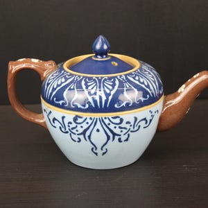 May include: A blue and white ceramic teapot with a brown handle and spout. The teapot has a floral design and is decorated with blue and white accents.