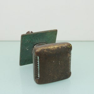 以下が含まれることがあります： 緑色の金属製の台座が付いた正方形の真鍮製のドアノブ。ノブの縁には装飾的な縁取りが施されています。