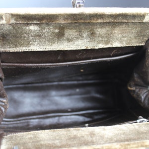 May include: Inside view of a vintage green velvet handbag with a brown fabric lining. The bag has a metal clasp closure and a zippered pocket.