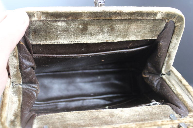 May include: Inside view of a vintage green velvet handbag with a brown fabric lining. The bag has a metal clasp closure and a zippered pocket.