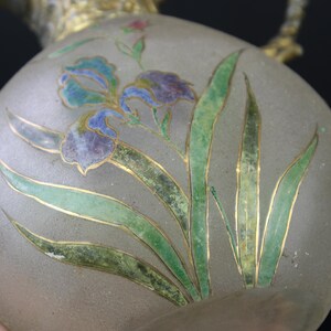 May include: A frosted glass vase with a floral design. The vase is decorated with green, blue, and gold painted leaves and flowers.