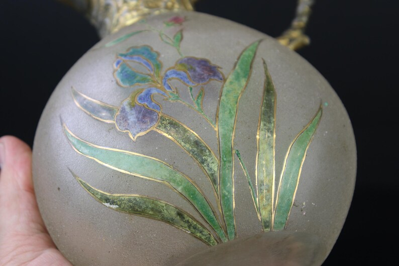May include: A frosted glass vase with a floral design. The vase is decorated with green, blue, and gold painted leaves and flowers.