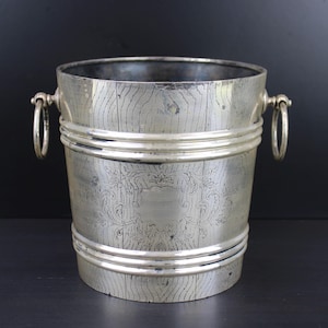 May include: A silver ice bucket with two handles. The bucket has a textured surface and a decorative design.