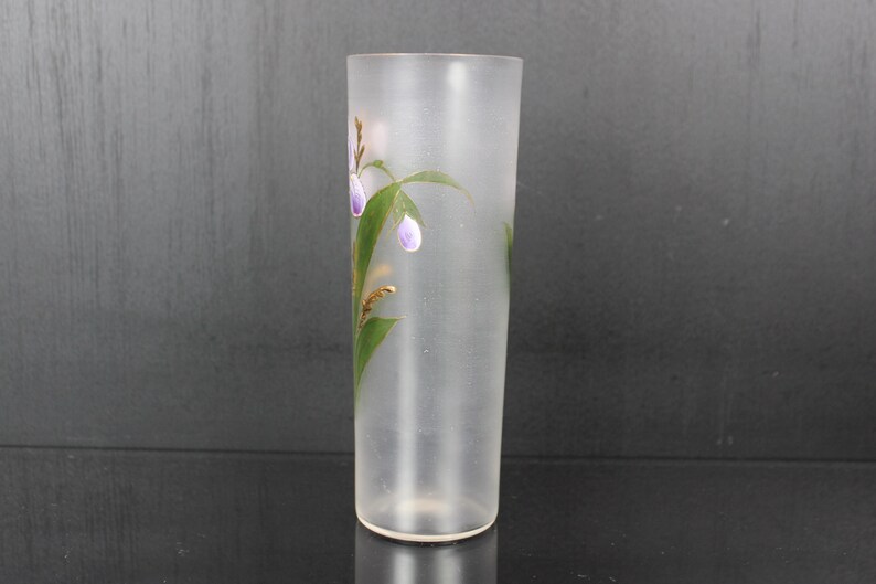 Pu&ograve; includere: Un vaso di vetro smerigliato di forma cilindrica. Il vaso &egrave; decorato con fiori viola dipinti a mano, foglie verdi e dettagli dorati. Il vaso &egrave; alto circa 20 cm.