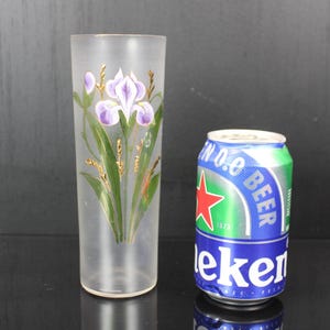 Pu&ograve; includere: Un bicchiere alto e smerigliato con un motivo a iris dipinto a mano in viola, verde e oro. Accanto, una lattina di birra Heineken. Il bicchiere &egrave; alto circa 20 cm.