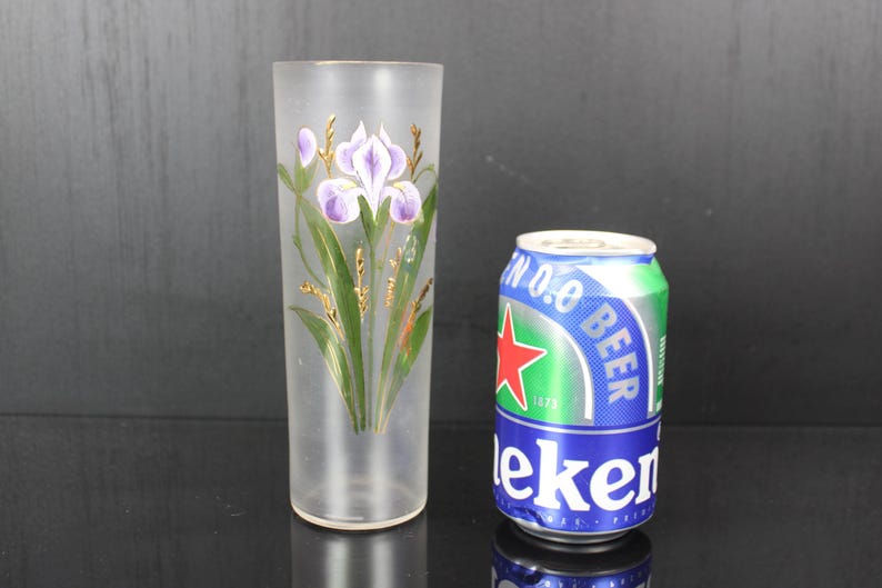 Pu&ograve; includere: Un bicchiere alto e smerigliato con un motivo a iris dipinto a mano in viola, verde e oro. Accanto, una lattina di birra Heineken. Il bicchiere &egrave; alto circa 20 cm.