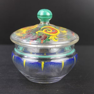 Puede incluir: Un tarro de vidrio transparente con tapa, pintado a mano con diseños florales y geométricos en amarillo, rojo, verde y azul.