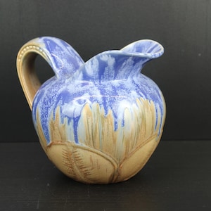 Puede incluir: Una jarra de cerámica azul y marrón con un diseño texturizado de hojas. La jarra tiene un cuerpo ancho y redondeado y un pico curvo.