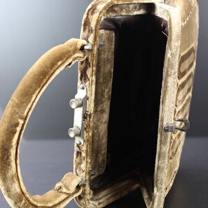 May include: A brown velvet handbag with a top handle and a metal clasp. The bag is open and the inside is lined with brown fabric.