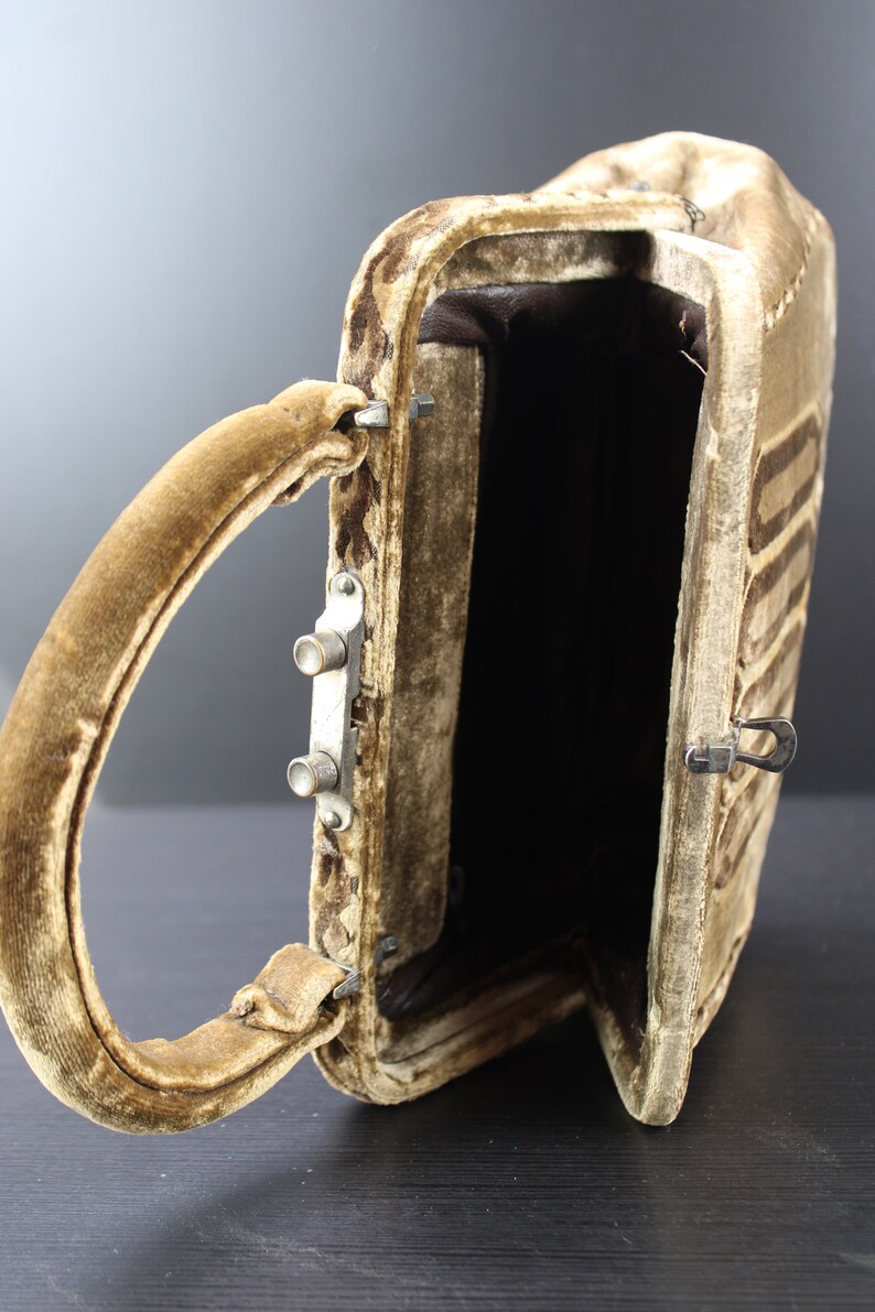 May include: A brown velvet handbag with a top handle and a metal clasp. The bag is open and the inside is lined with brown fabric.