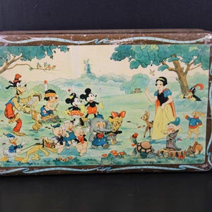 May include: Vintage rectangular tin featuring a colorful illustration of Disney characters, including Mickey and Minnie Mouse, Snow White, and Goofy. The artwork depicts a pastoral scene with trees, a windmill, and various animals. The tin has a brown border.