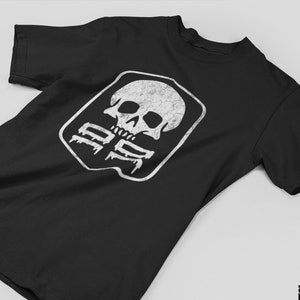 May include: Black t-shirt featuring a white distressed graphic of a skull inside a diamond shape. The graphic includes the text "100%" within the diamond.