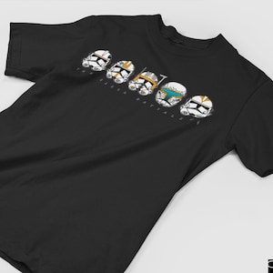 Puede incluir: Camiseta negra con un gráfico blanco de seis cascos de soldados clon de Star Wars. Los cascos están alineados en una fila y tienen diferentes marcas de colores. El texto "The Bad Batch" está impreso debajo de los cascos.