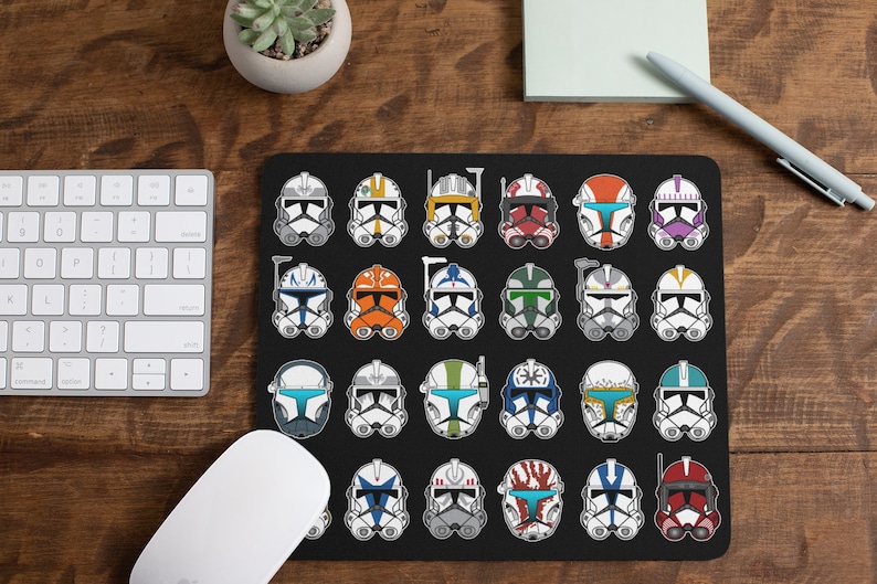 K&ouml;nnte beinhalten: Eine schwarze Mausmatte mit einem Raster aus 36 bunten Star Wars Klonkrieger-Helmen. Jeder Helm hat ein einzigartiges Farbschema und Design.