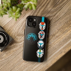 May include: Black phone case featuring a series of colorful helmet designs and a blue emblem. The case has a vertical blue stripe and is set against a wooden background. The helmets are red, white, blue, and green.