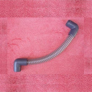 May include: A gray, flexible hose with two dark gray elbow connectors. The hose is corrugated and curved, lying on a pink textured surface. The connectors are at each end of the hose.