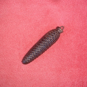 May include: A dark brown, cone-shaped object with a metal loop at the top, likely a clock weight. The object has a textured, woven appearance and is set against a red background.