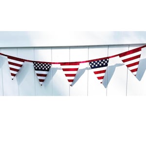 May include: A patriotic bunting banner with alternating red and white striped pennants and pennants with a blue field of white stars. The banner is strung on a red ribbon and hangs against a white background.