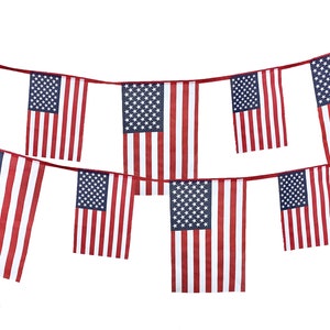 May include: A string of red, white, and blue American flags hanging against a white background. The flags are made of fabric and have a star pattern.