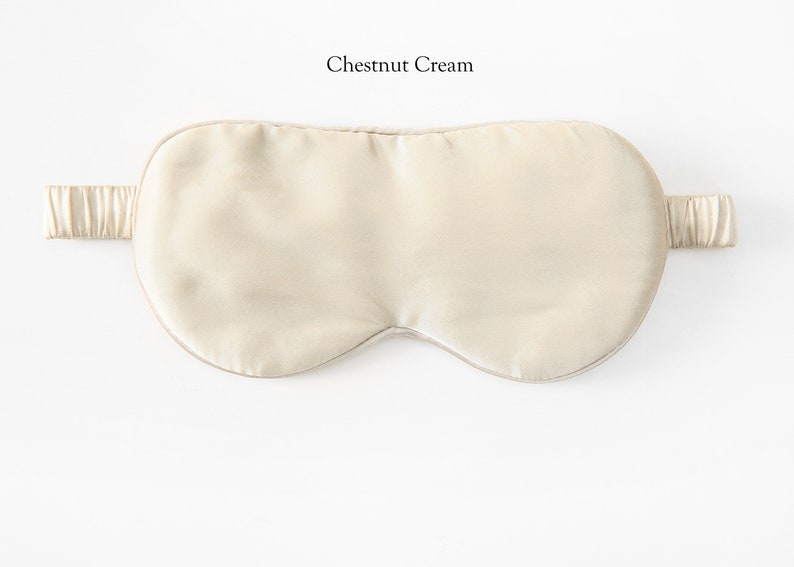 May include: A light beige silk sleep mask with an elastic strap. The mask is designed to block out light and promote sleep.