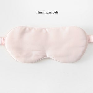 May include: A pale pink satin sleep mask with an adjustable strap. The mask is designed to block out light and promote sleep.