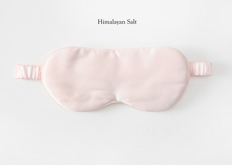 May include: A pale pink satin sleep mask with an adjustable strap. The mask is designed to block out light and promote sleep.