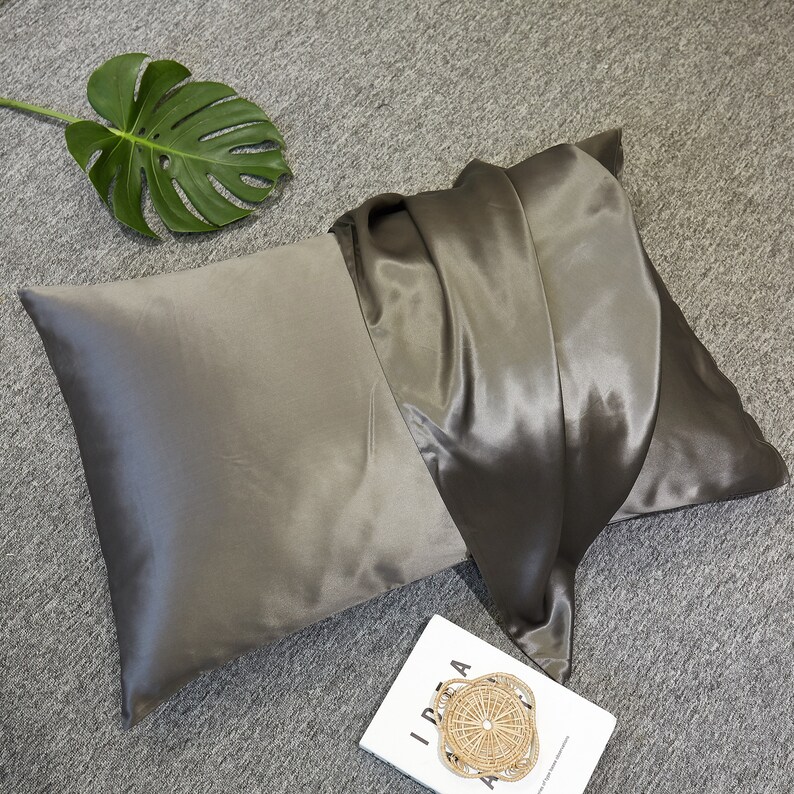 May include: A gray satin pillowcase with a folded edge. The pillowcase is made of soft, luxurious satin and is perfect for sleeping on.