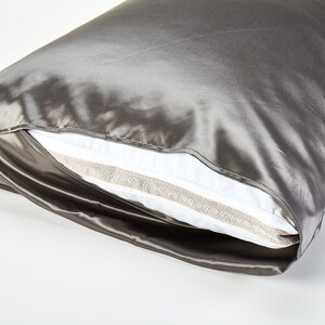 May include: A gray satin pillowcase with a white pillow inside. The pillowcase has a decorative trim around the edge.