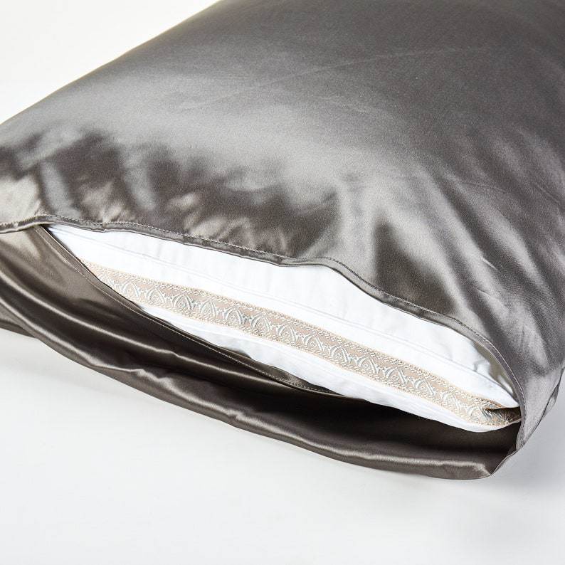 May include: A gray satin pillowcase with a white pillow inside. The pillowcase has a decorative trim around the edge.