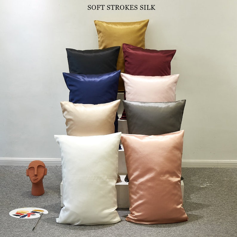 May include: A stack of eight pillowcases in various colors, including gold, black, navy blue, burgundy, pink, beige, gray, and peach. The pillowcases are made of soft silk and are arranged in a pyramid shape. The text "SOFT STROKES SILK" is displayed at the top of the image.