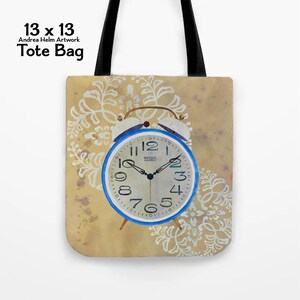 May include: Tote bag featuring a vintage-style alarm clock with a blue frame and white face. The clock is set against a beige background with white floral patterns. The bag is 13 x 13 inches.