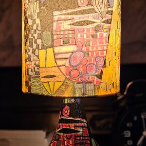 May include: A table lamp with a colorful, abstract patterned lampshade and a similarly patterned base. The lampshade is cylindrical and the base is shaped like a pear.