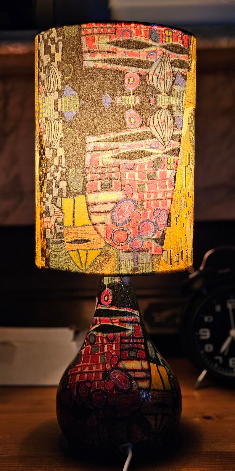 May include: A table lamp with a colorful, abstract patterned lampshade and a similarly patterned base. The lampshade is cylindrical and the base is shaped like a pear.