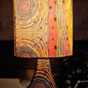 May include: A table lamp with a colorful, abstract patterned lampshade and a pear-shaped base with a similar pattern. The lamp is on a wooden surface.