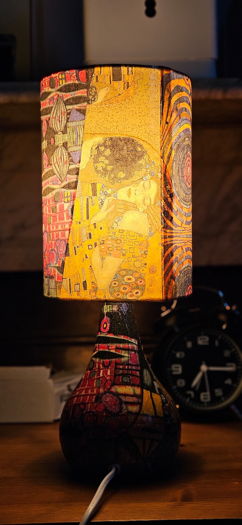 May include: A table lamp with a colorful, patterned lampshade featuring a painting of two people embracing. The lamp base is also decorated with a colorful, geometric pattern.