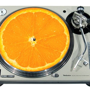 Puede incluir: Un tocadiscos plateado con una rodaja de fruta naranja brillante en el plato. El tocadiscos tiene una aguja negra y un brazo de tono plateado. El texto "Technics" es visible en el tocadiscos.