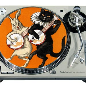 Könnte beinhalten: Eine schwarze Katze und ein weißes Kaninchen spielen Banjo auf orangefarbenem Hintergrund. Das Bild ist eine Plattenteller-Slipmat.