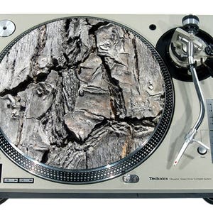 Può includere: Giradischi Technics SL-1200MK3D argentato con un design a venature del legno sul piatto. Il giradischi presenta un braccio, controllo del pitch e pulsanti start/stop. Il piatto ha un aspetto di corteccia d'albero strutturata.
