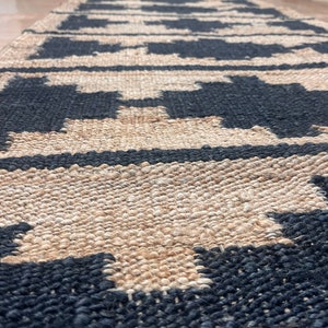 May include: A black and natural jute rug with a geometric pattern. The rug has a woven texture and is made of natural fibers.