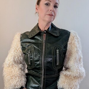 May include: A dark green jacket with cream-colored, fluffy sleeves. The jacket has a zipper closure, two zippered pockets, and white stitching. The collar is a classic style.