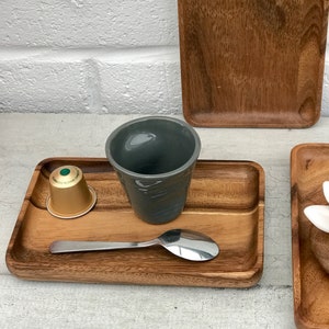 May include: A wooden tray with a grey ceramic cup, a silver spoon, and a single-serve coffee pod. The tray is made of acacia wood and has a natural finish.
