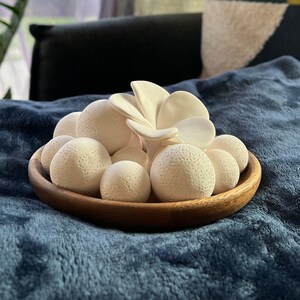 May include: A wooden bowl filled with white ceramic spheres and a white ceramic flower. The bowl is on a blue fuzzy surface.